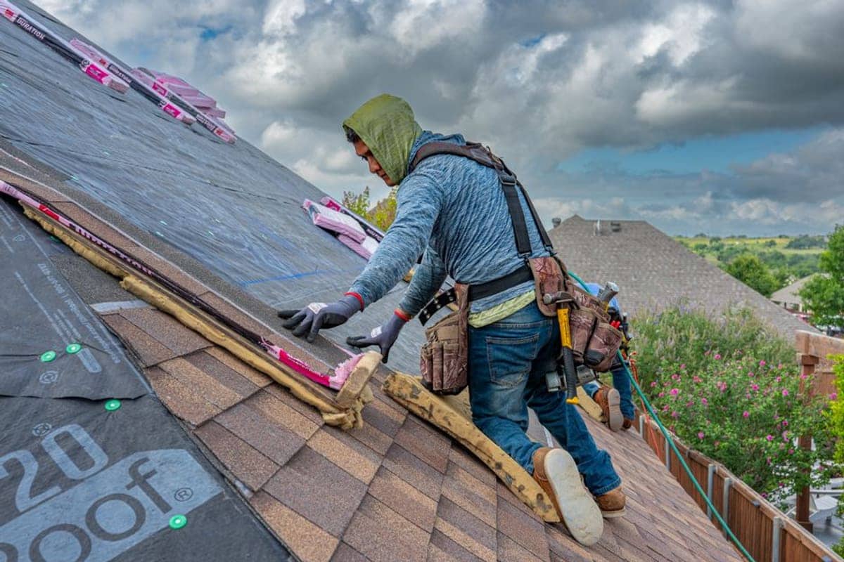 A licensed roofer carrying shingles across a new residential roof