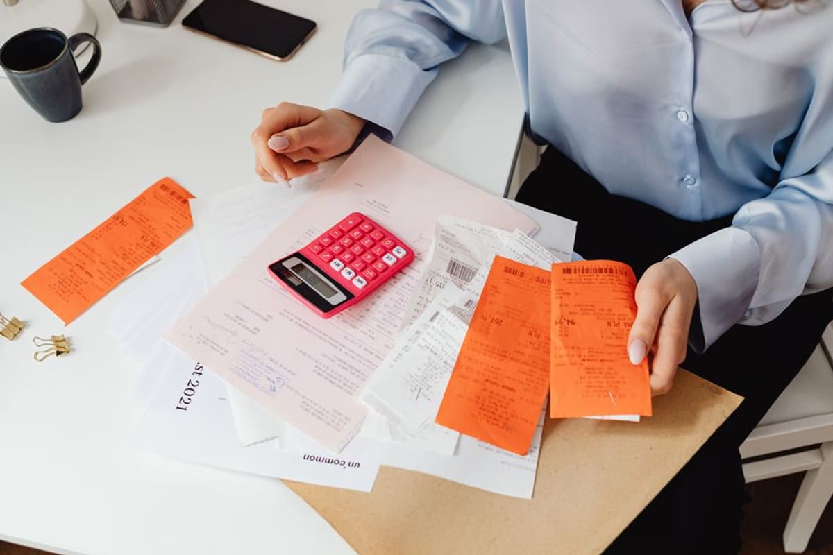 A person sorting through bills and receipts with a calculator